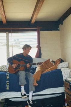 a man sitting on top of a bed while holding a guitar