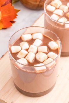 two cups filled with hot chocolate and marshmallows on top of a cutting board