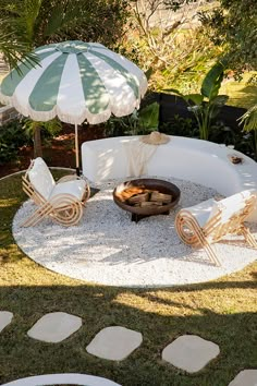 an outdoor fire pit with chairs and umbrellas in the middle of it, surrounded by grass