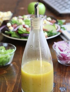 a bottle filled with dressing sitting on top of a wooden table next to plates of salad