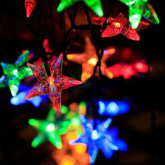 multicolored star shaped lights are hanging from a tree branch in the night time