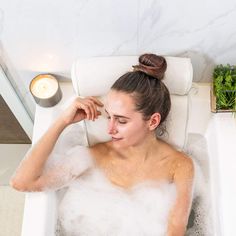 a woman sitting in a bathtub with foam on her face and hair pulled back