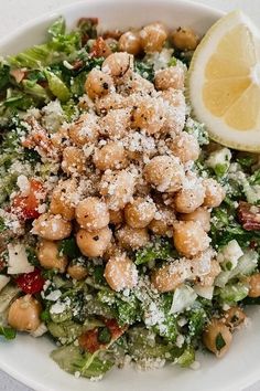 a white bowl filled with salad covered in nuts and cheese next to a lemon wedge