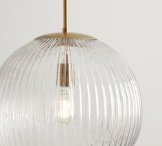 a clear glass ball light hanging from a gold colored ceiling fixture with a white wall in the background