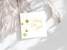 a white card with gold foil lettering on it next to some palm leaves and branches