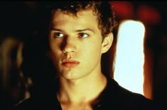 a young man with curly hair and blue eyes looks into the camera while wearing a black shirt