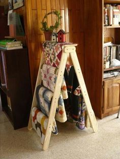 a wooden ladder holding quilts and blankets in a room with bookshelf behind it