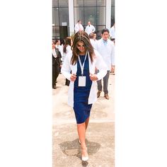 a woman in a blue dress and white jacket walking down the street with other people behind her