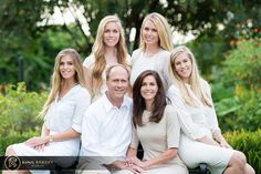 a group of people sitting on top of a bench in front of some bushes and trees