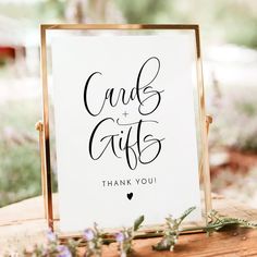 a card and gifts sign sitting on top of a wooden table next to purple flowers