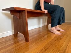 a woman sitting on top of a wooden bench in front of a white wall and hardwood floor