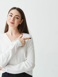 a woman pointing to the side with her hand on her hip and wearing a white shirt