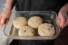 four cookies in a glass dish being held by a person with an apron over their shoulder