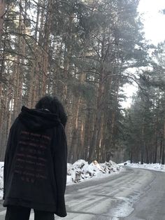 a person standing on the side of a snowy road in front of some tall trees