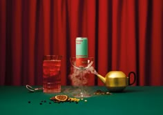 a green table topped with two glasses and a tea pot next to a red curtain