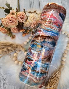 a large glass tube sitting on top of a white table next to flowers and feathers