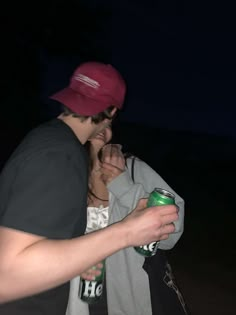 a man and woman standing next to each other at night with one holding a can