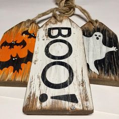 three wooden halloween tags with bats and ghostes hanging from twine strings on a white wall