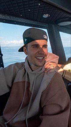 a man sitting in the back seat of a boat smiling at the camera while wearing a hat