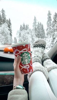 someone is holding a cup in their hand while driving through the snow covered mountains and trees