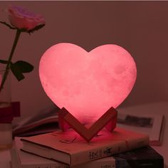 a pink heart shaped lamp sitting on top of a stack of books next to a rose