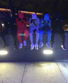 several people sitting on a wall with their feet up in the air at night time