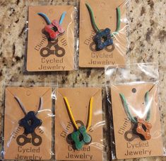 four different colored scissors in plastic bags on a counter top with tags attached to them