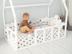 a baby sitting on top of a white bed with stars and pillows in it's canopy