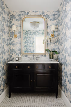 a bathroom with blue and white wallpaper has a large mirror above the sink, along with two lamps on either side of the vanity