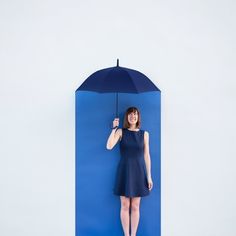 a woman standing in front of a blue wall holding an umbrella