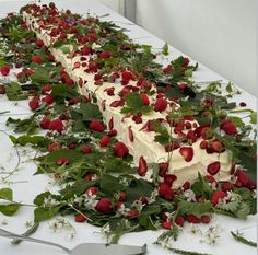 there is a long cake with strawberries on it and flowers all over the table