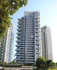 the tall building has many balconies on it's sides and is surrounded by other high rise buildings