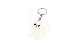 a white keychain with a cat on it's back and black eyes