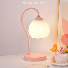 a pink lamp sitting on top of a table next to a cup and saucer