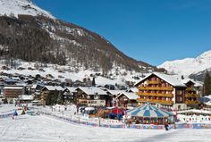 a ski resort in the mountains with snow on the ground and people walking around it