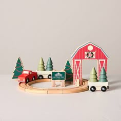 a wooden toy train set with trees and a red barn in the background on a white surface