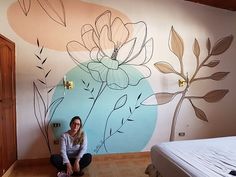 a woman sitting on the floor in front of a painted wall with flowers and leaves