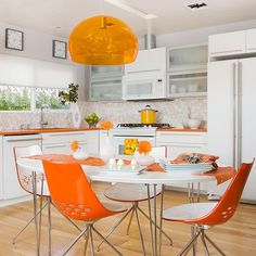 a kitchen with white cabinets and orange chairs around a table in the middle of the room