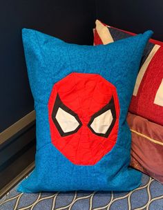 a spiderman pillow sitting on top of a bed next to two pillows with eyes