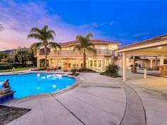 a large house with a swimming pool in the front yard and palm trees around it