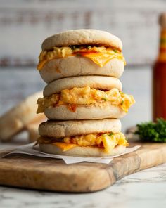 three sandwiches stacked on top of each other with eggs and cheese in between them, sitting on a cutting board