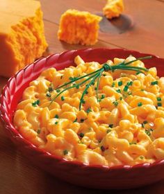 a red bowl filled with macaroni and cheese on top of a wooden table