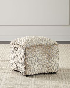 a square ottoman sitting on top of a carpeted floor next to a white wall