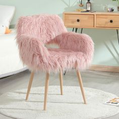 a pink chair sitting on top of a white rug next to a wooden table and dresser