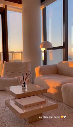 a living room filled with white furniture and large windows overlooking the ocean at sunset or dawn