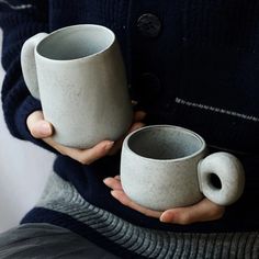 two white mugs are held in their hands