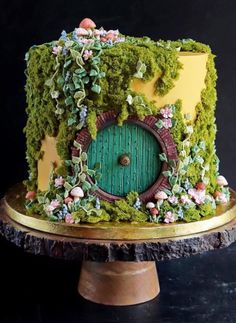 a cake decorated with moss and flowers on a wooden stand in front of a black background