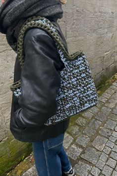 a woman in black jacket carrying a blue and white handbag on brick sidewalk next to wall