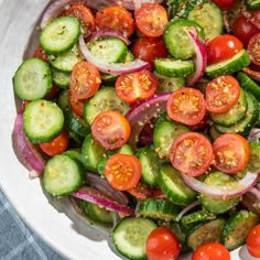 a white bowl filled with cucumbers, tomatoes and onion salad on top of a blue table cloth