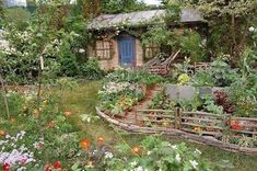 a garden with lots of flowers and plants in front of a small building that has a blue door